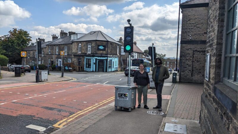 Photograph of Cllrs Ruth Milsom and Minesh Parekh, standing next to the temporary traffic light crossing at Crookes near the junction with School Road. 